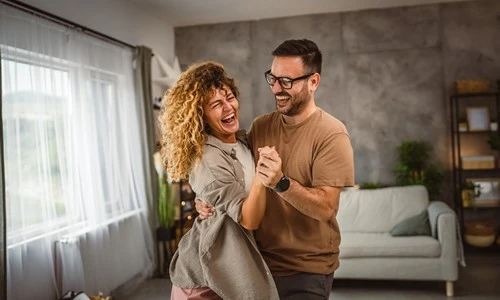 Couple heureux en train de danser dans leur salon après avoir acheté leur maison avec un prêt immobilier
