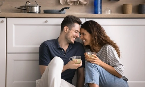 Coppia seduta per terra che beve un caffè nella propria casa acquistata con un mutuo ipotecario. Sono felici.